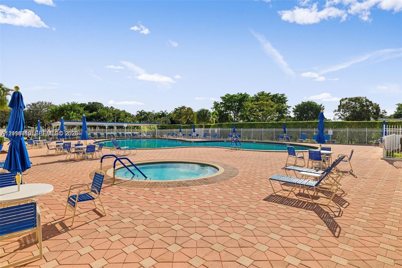 Community swimming pool and integrated spa featuring decorative paver decking and perimeter privacy fencing