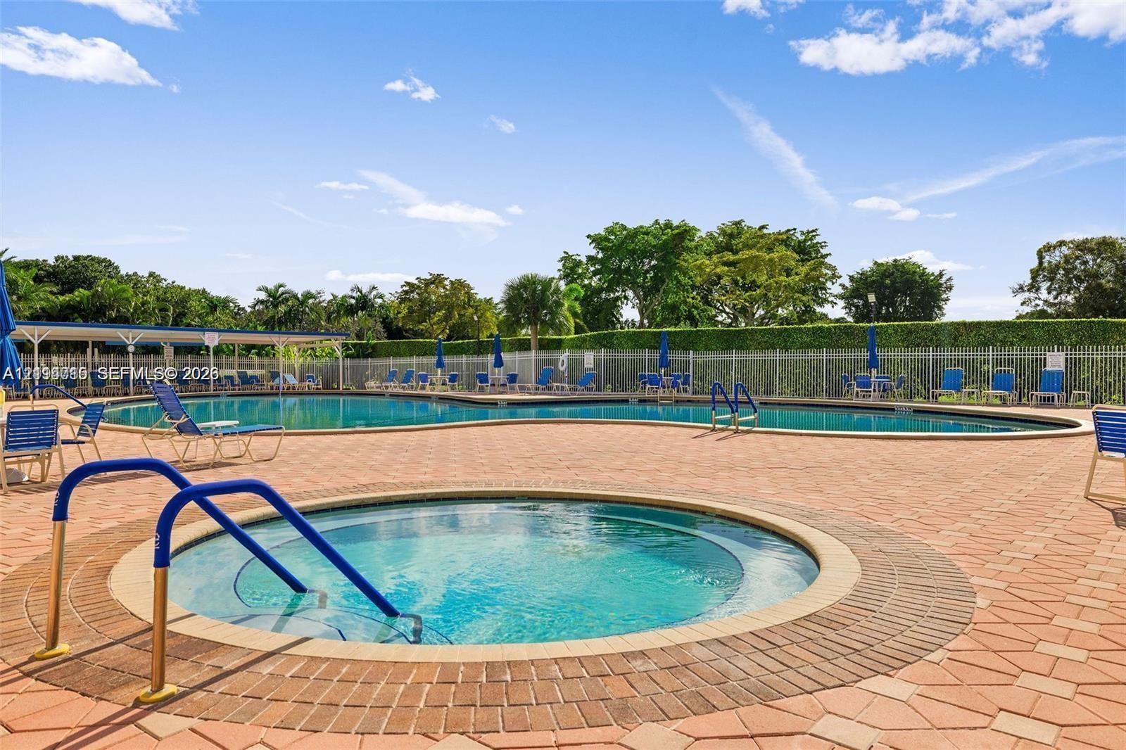 Swimming pool and spa with paver deck surround, metal safety railing, and perimeter privacy hedge