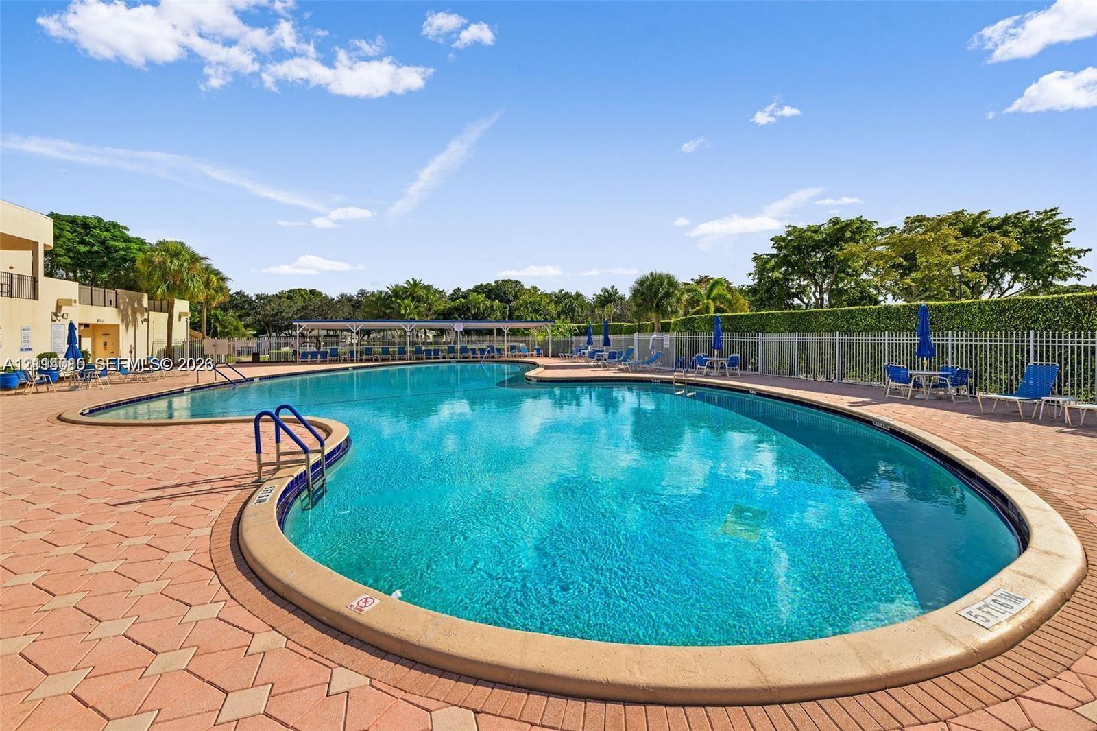 Freeform swimming pool with a tiled perimeter, integrated metal handrails, and surrounding brick-paver decking enclosed by perimeter fencing