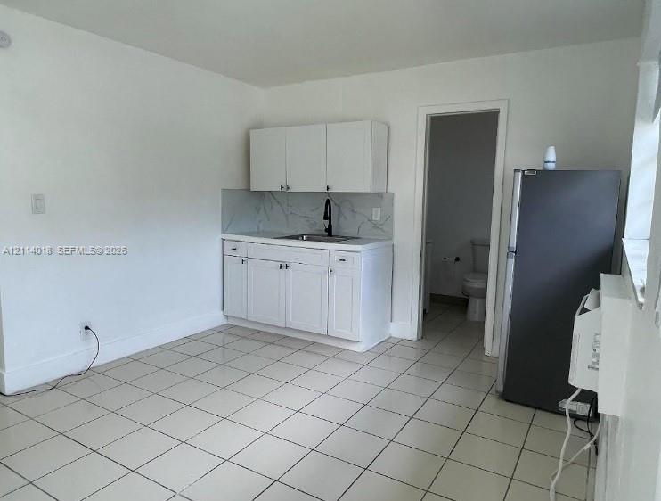 Kitchenette featuring white cabinetry, stone-patterned backsplash, stainless steel sink, matte black gooseneck faucet, and tile flooring