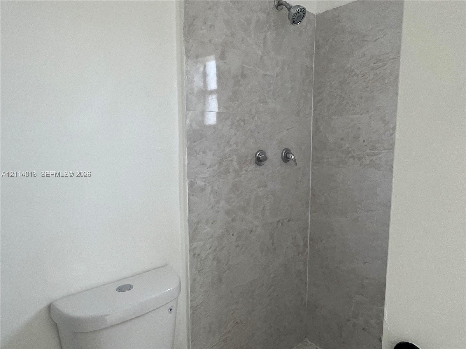Walk-in shower enclosure featuring large-format grey stone-finish tile surround, wall-mounted shower head, and chrome-finish plumbing fixtures