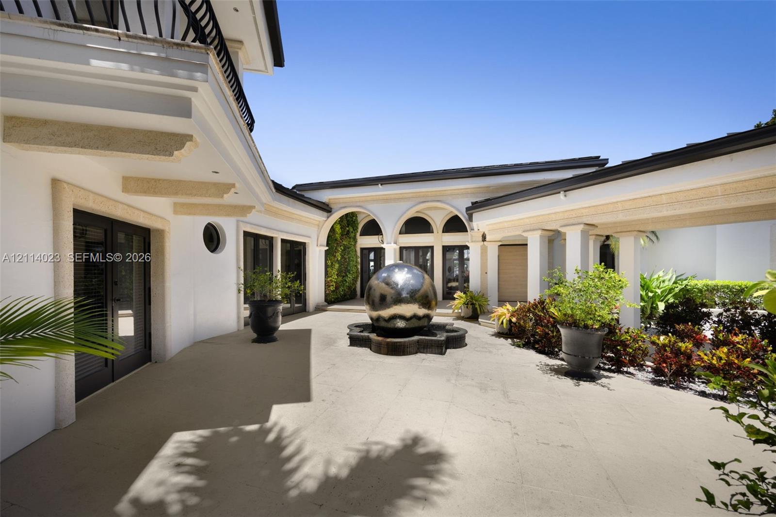 Enclosed courtyard featuring a central spherical water feature, stone-paved patio, covered walkway with arched columns, and exterior glass-paneled doors