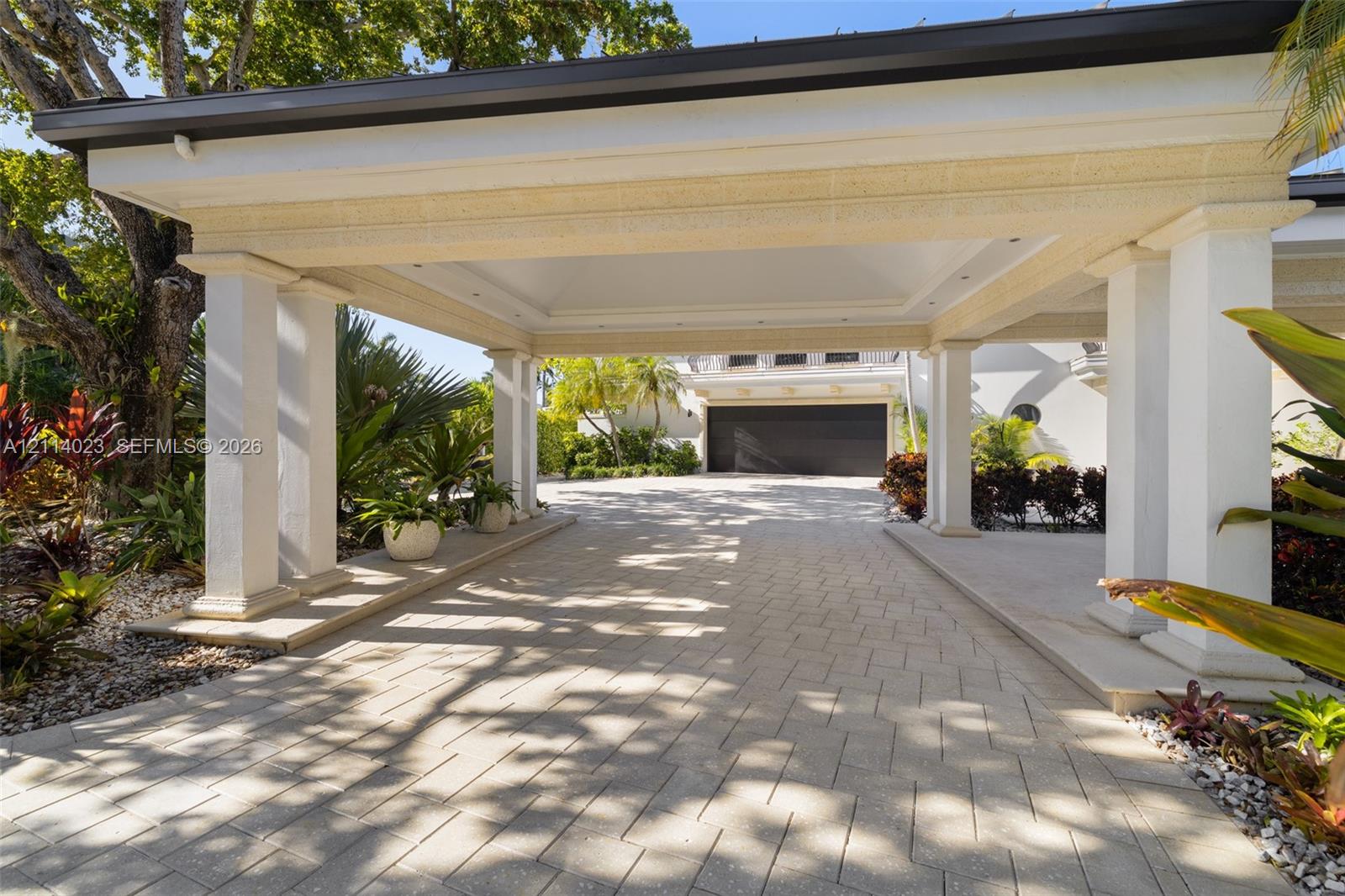 Covered porte-cochere featuring structural columns, recessed lighting, and a paved stone driveway leading to a multi-car garage Covered porte-cochere featuring structural columns, recessed lighting, and a paved stone driveway leading to a multi-car garage