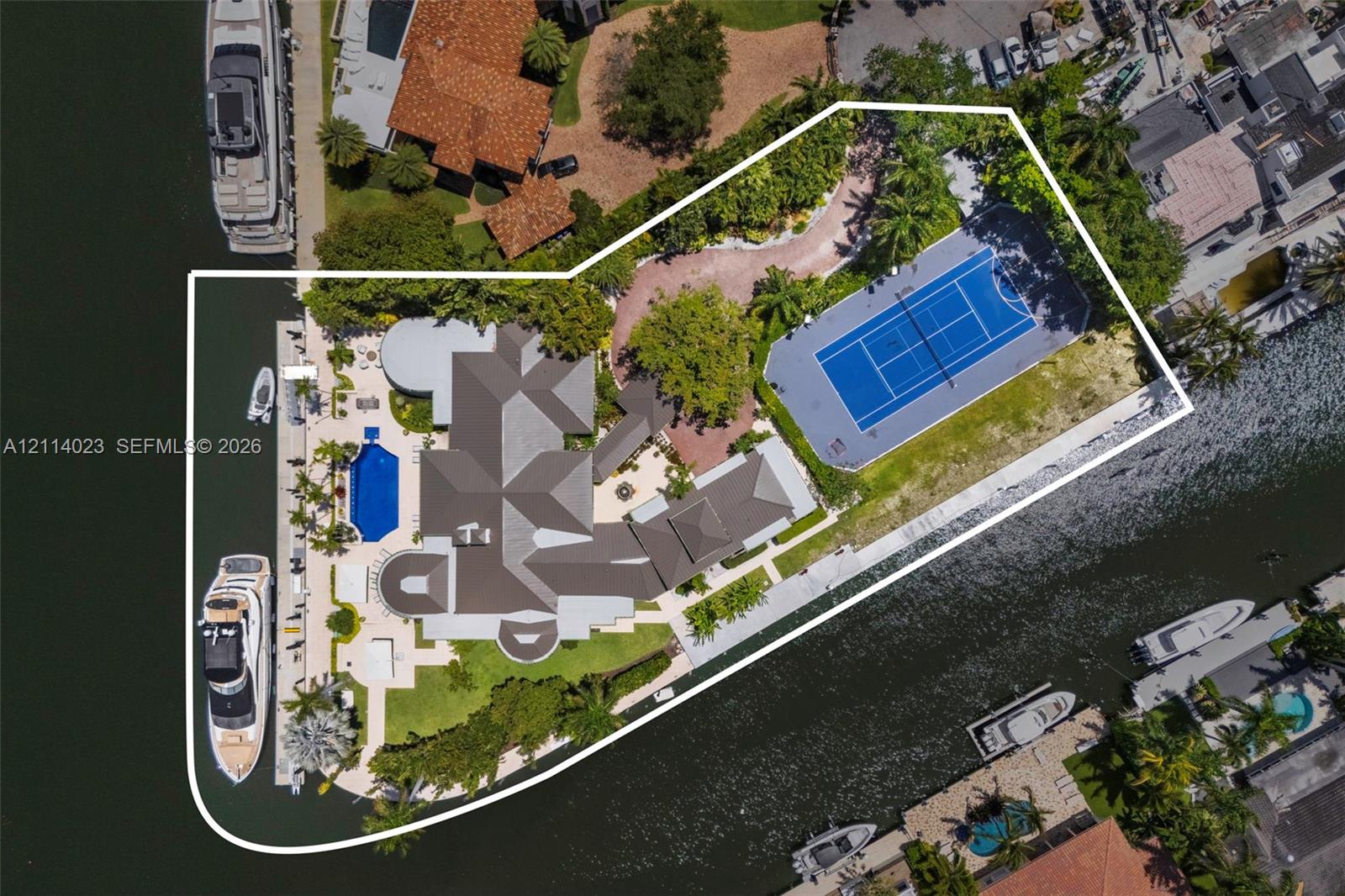 Waterfront estate featuring a private deep-water dock, tennis court, swimming pool, and expansive hardscaped grounds with mature landscaping