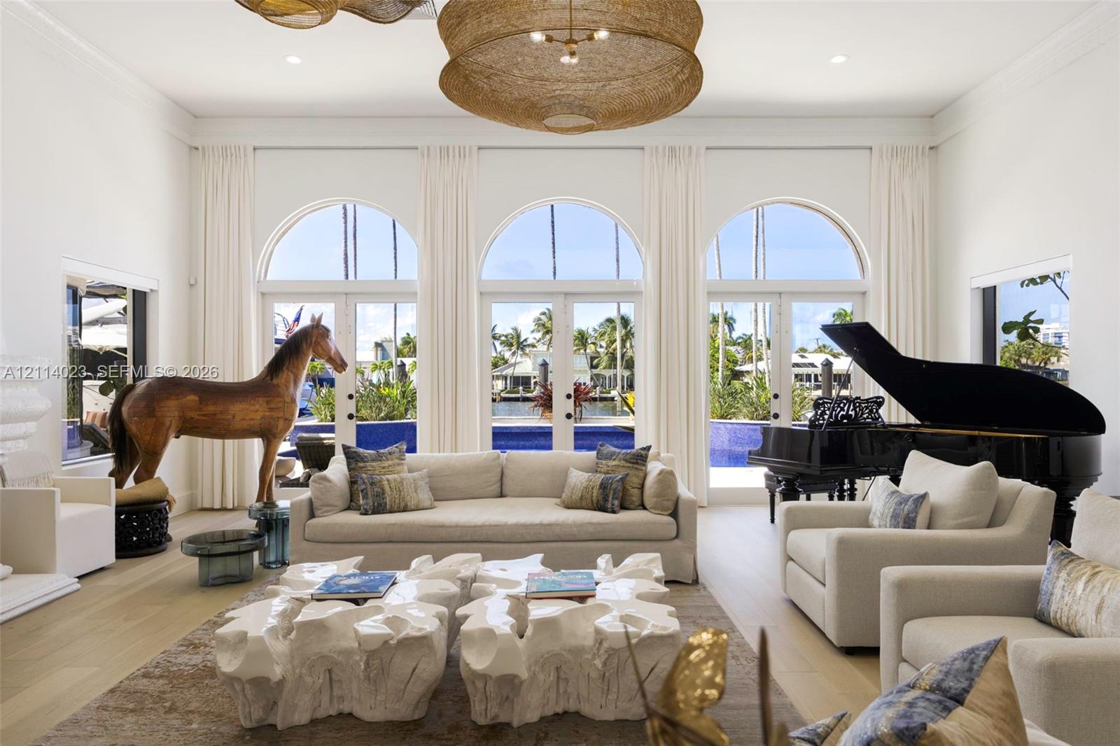 High-ceiling living area featuring three sets of floor-to-ceiling arched glass doors, light wood-finish flooring, recessed lighting, and oversized woven pendant light fixtures