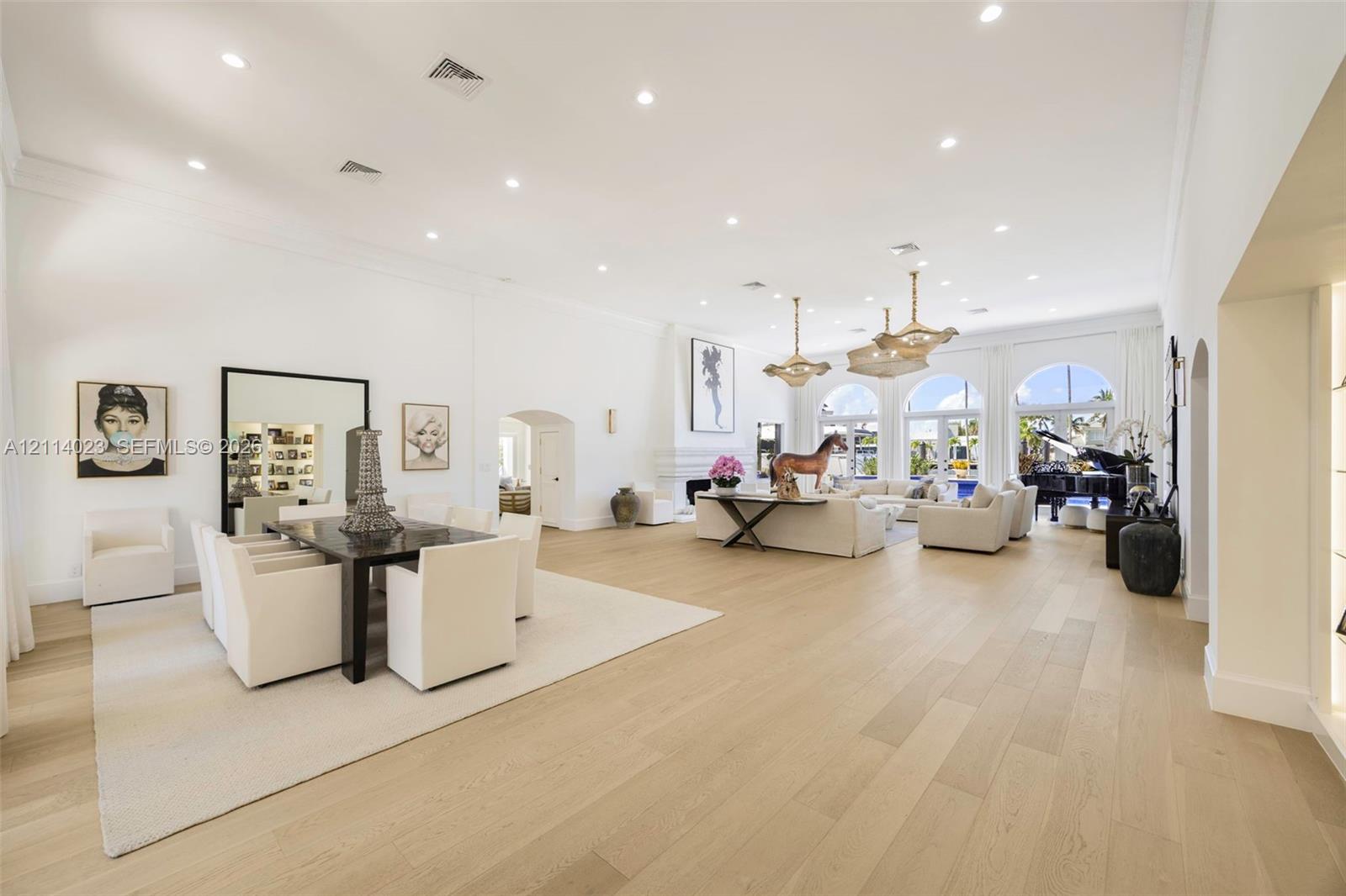 Expansive living area featuring high ceilings with recessed lighting, wood-finish flooring, three arched floor-to-ceiling windows, and decorative pendant light fixtures