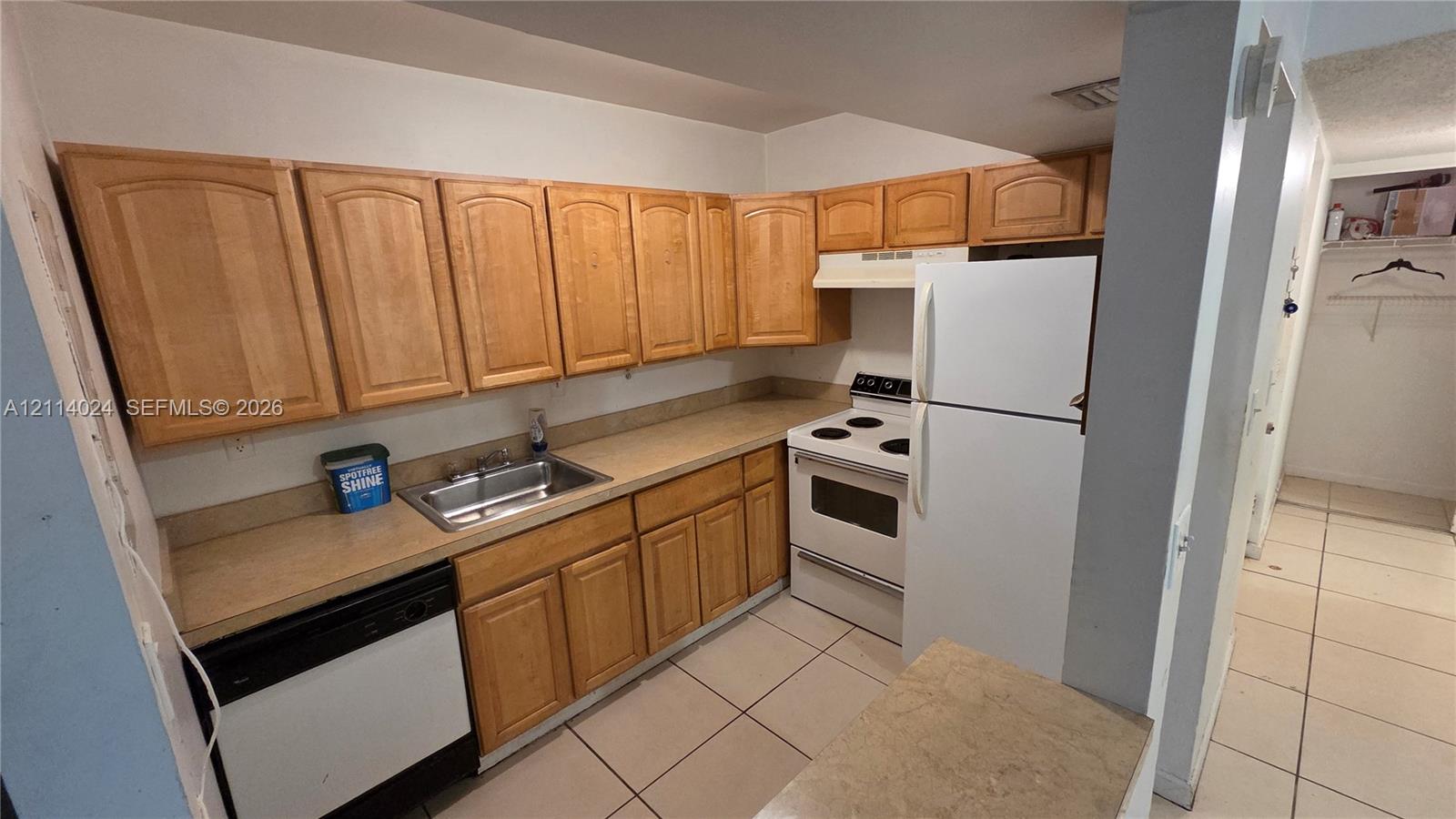 Kitchen featuring wood cabinetry, integrated stainless steel sink, solid-surface countertops, and tile flooring Kitchen featuring wood cabinetry, integrated stainless steel sink, solid-surface countertops, and tile flooring