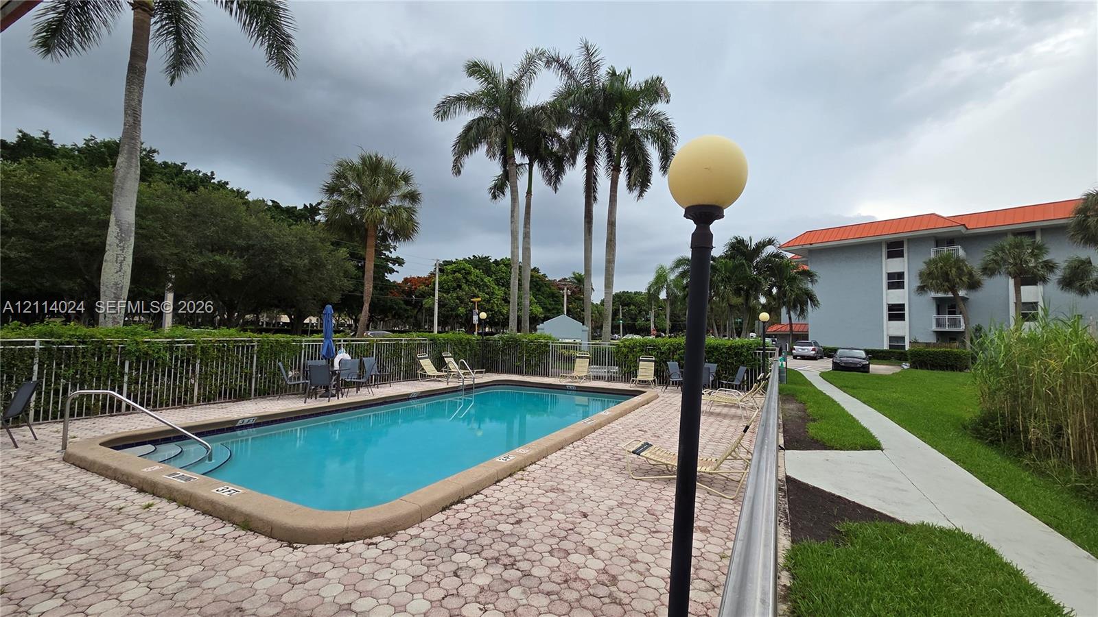 Swimming pool featuring a concrete paver deck, metal perimeter fencing, and mature palm trees