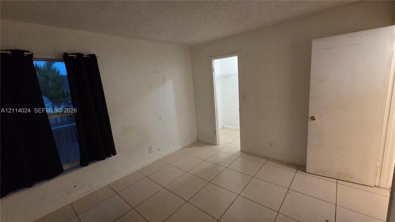 Neutral-toned interior space featuring light-colored tile flooring, a window, and a door providing entry to a storage closet Neutral-toned interior space featuring light-colored tile flooring, a window, and a door providing entry to a storage closet