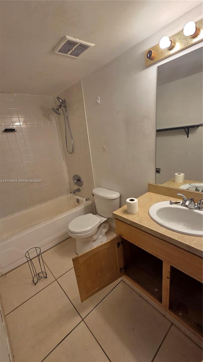 Full bathroom featuring large-format floor tile, a soaking tub with integrated shower head, vanity with countertop basin, and wall-mounted vanity lighting Full bathroom featuring large-format floor tile, a soaking tub with integrated shower head, vanity with countertop basin, and wall-mounted vanity lighting