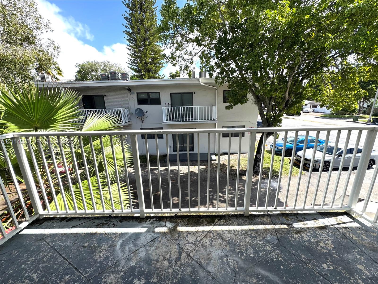 Private balcony featuring white metal railings and concrete flooring with mature palm and broadleaf trees