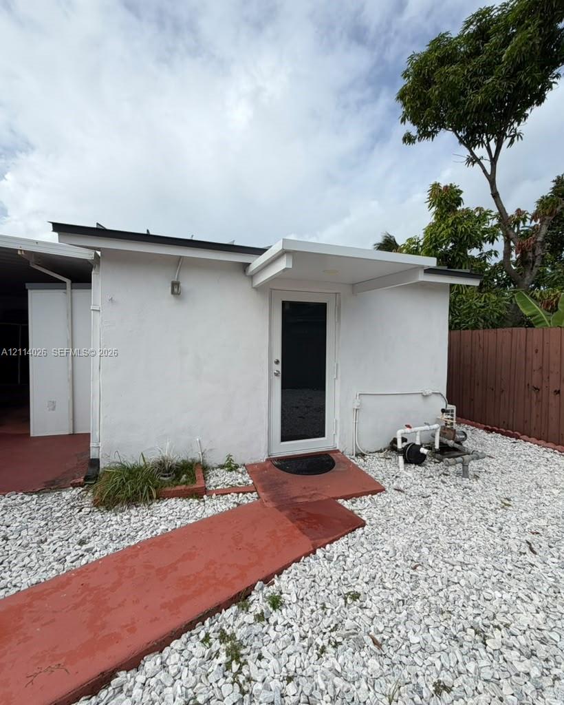 Exterior area featuring white stucco siding, a paved walkway, light-toned stone ground cover, and a covered entryway