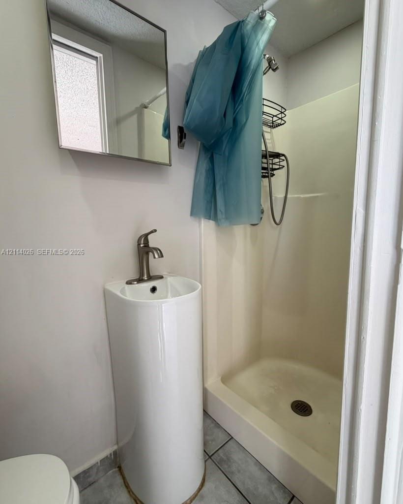 Wall-mounted rectangular mirror, pedestal sink with a single-handle brushed nickel faucet, and a prefabricated shower stall