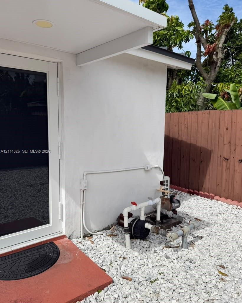 Exterior of the structure featuring white smooth-finish siding, a full-lite glass door, and a white gravel ground cover enclosed by a vertical wood-plank fence