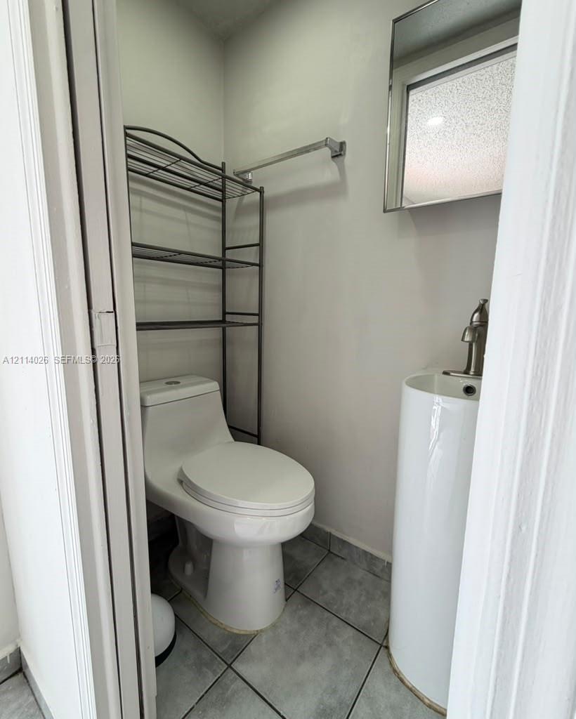 Compact restroom featuring a white pedestal sink with a single-handle faucet, a one-piece elongated toilet, and grey tile flooring