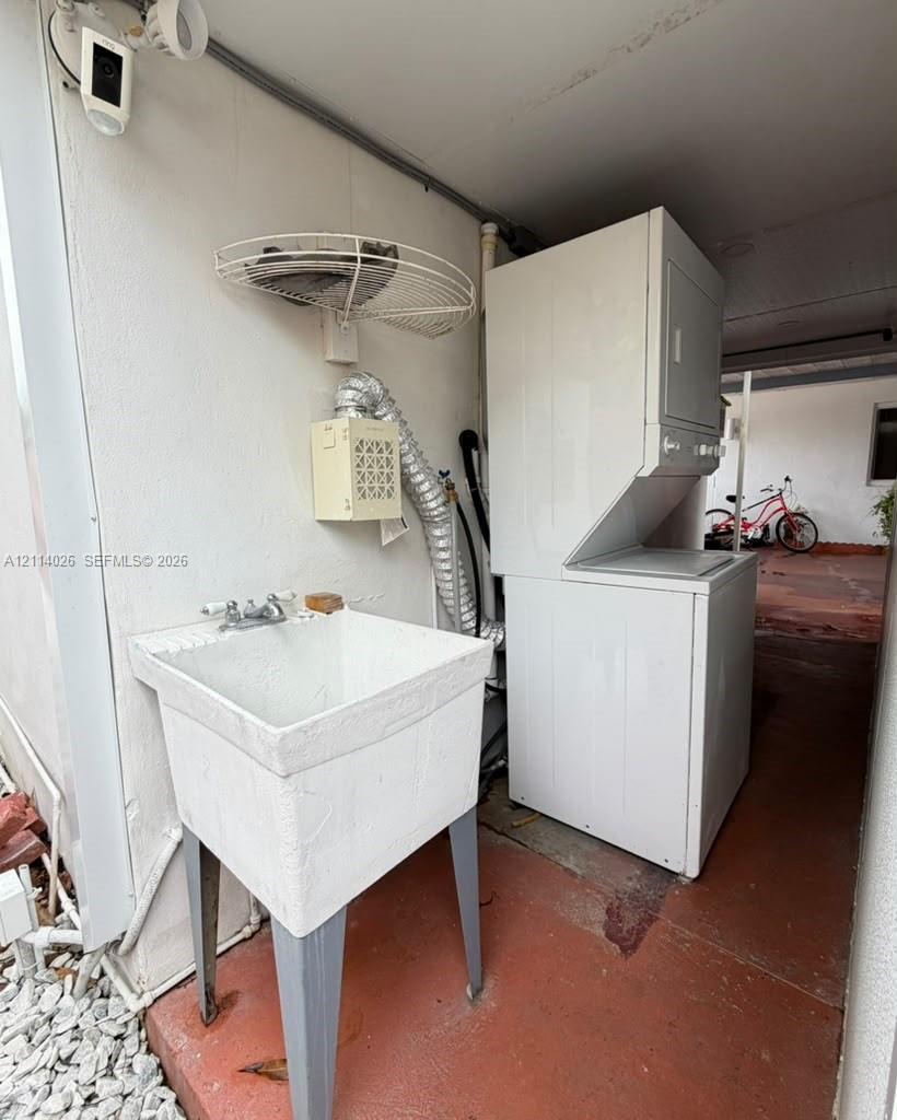 Utility area featuring a floor-mounted basin with dual-handle faucet, stackable laundry unit, wall-mounted wire shelf, and security camera