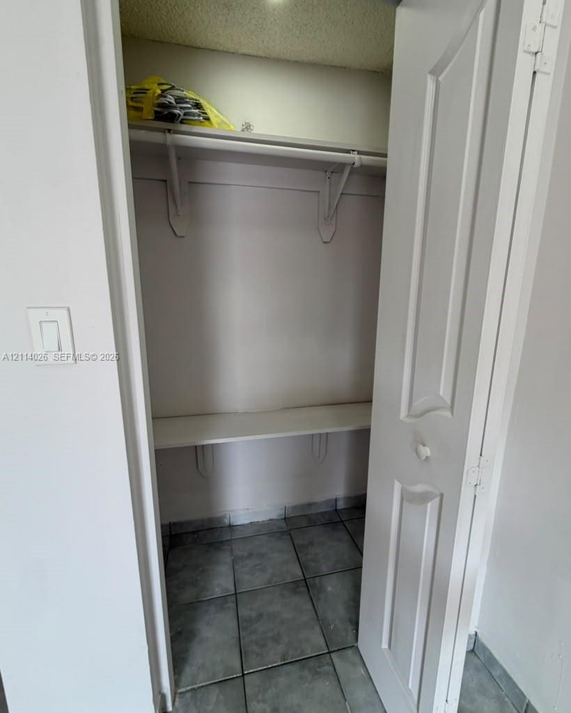 Storage closet featuring tile flooring, two-tiered built-in shelving, and a paneled door