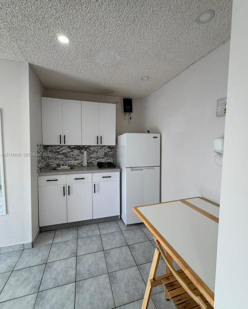 Kitchenette featuring white cabinetry, a stone-patterned backsplash, neutral countertops, recessed lighting, and ceramic tile flooring