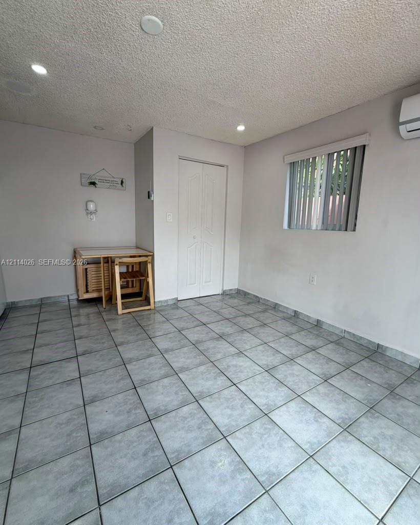 Interior room featuring neutral wall paint, recessed lighting, tile flooring, a wall-mounted ductless mini-split system, and a window with vertical blinds