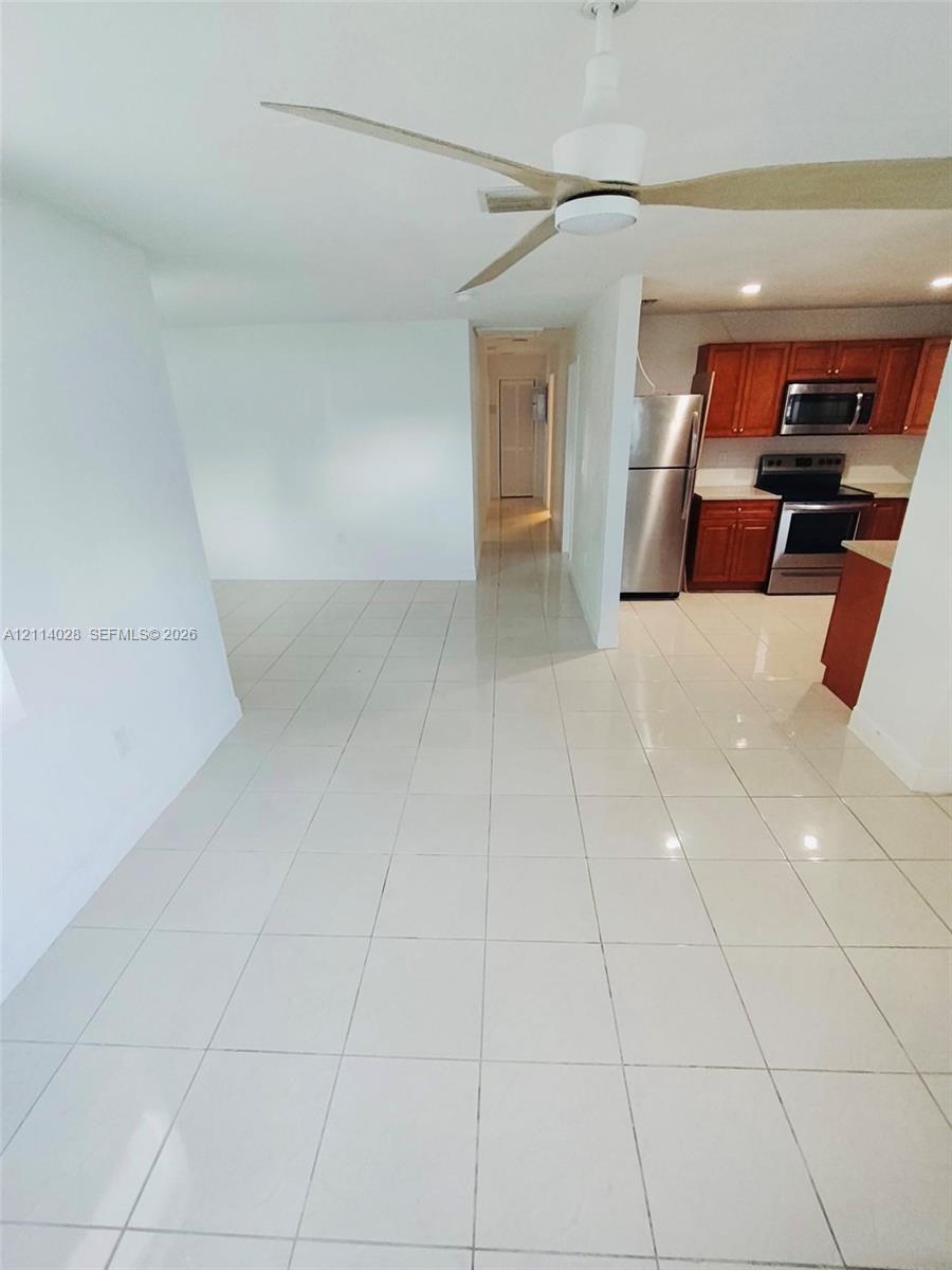 Neutral tile flooring, kitchen featuring wood cabinetry, stainless steel appliances, and ceiling fan with integrated lighting Neutral tile flooring, kitchen featuring wood cabinetry, stainless steel appliances, and ceiling fan with integrated lighting
