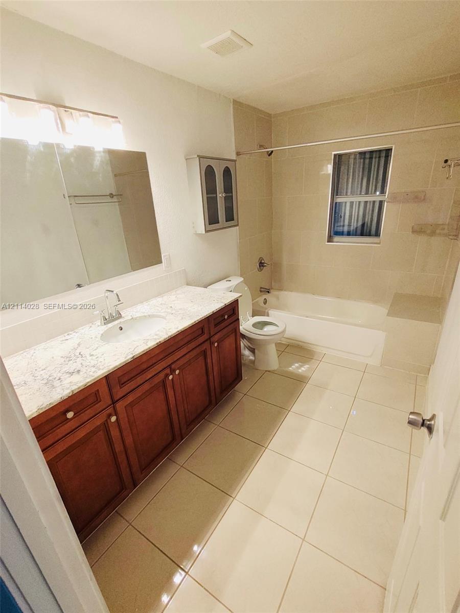 Full bathroom featuring a single-sink vanity with stone-patterned countertop, wood-finish cabinetry, tile flooring, and a tub-shower combination with tile surround