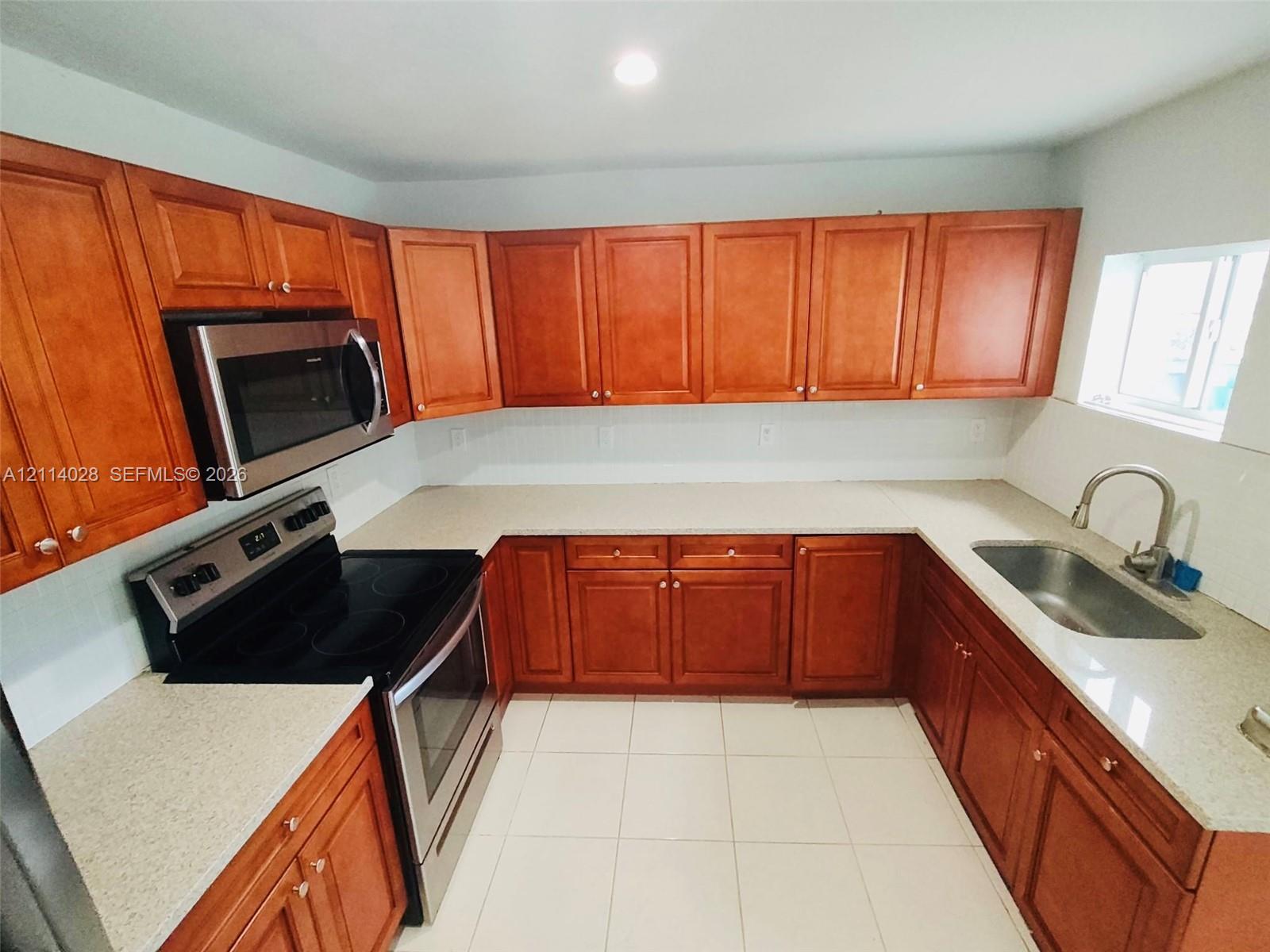 Kitchen featuring wood cabinetry, stone-composite countertops, stainless steel appliances, ceramic tile flooring, and a single-basin undermount sink Kitchen featuring wood cabinetry, stone-composite countertops, stainless steel appliances, ceramic tile flooring, and a single-basin undermount sink