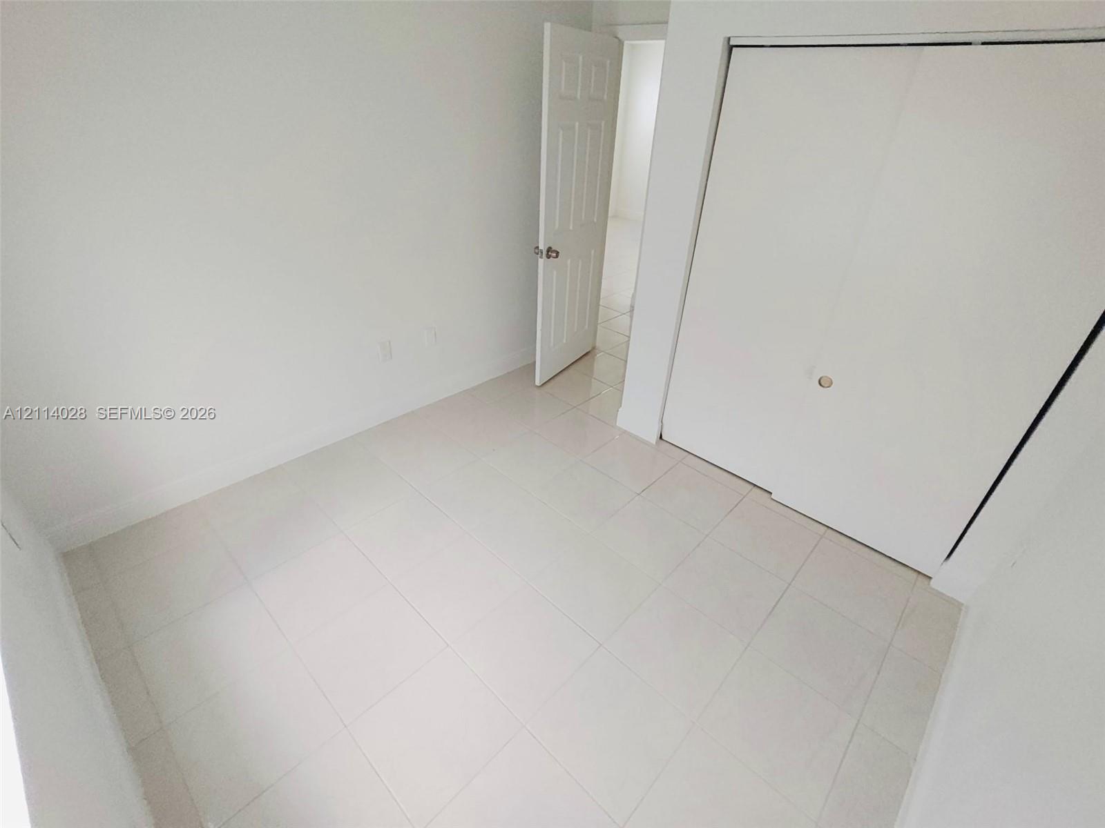 Interior space featuring white-toned tile flooring, neutral walls, a six-panel door, and a built-in closet with sliding doors Interior space featuring white-toned tile flooring, neutral walls, a six-panel door, and a built-in closet with sliding doors