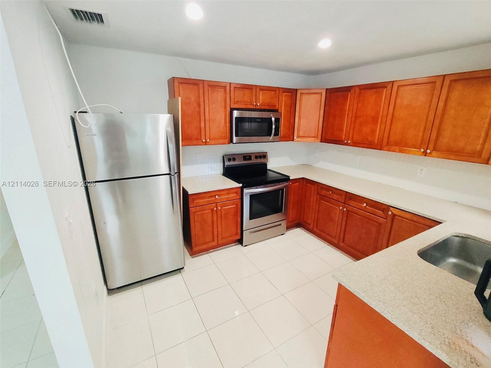 Kitchen featuring wooden cabinetry, solid surface countertops, stainless steel refrigerator, stainless steel microwave, and stainless steel electric range Kitchen featuring wooden cabinetry, solid surface countertops, stainless steel refrigerator, stainless steel microwave, and stainless steel electric range