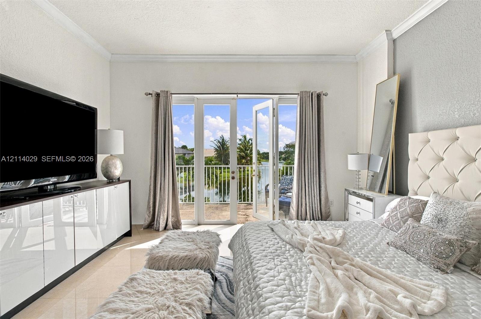 Double glass-paned doors opening to a private balcony, polished tile flooring, crisp crown molding, and built-in glossy white cabinetry