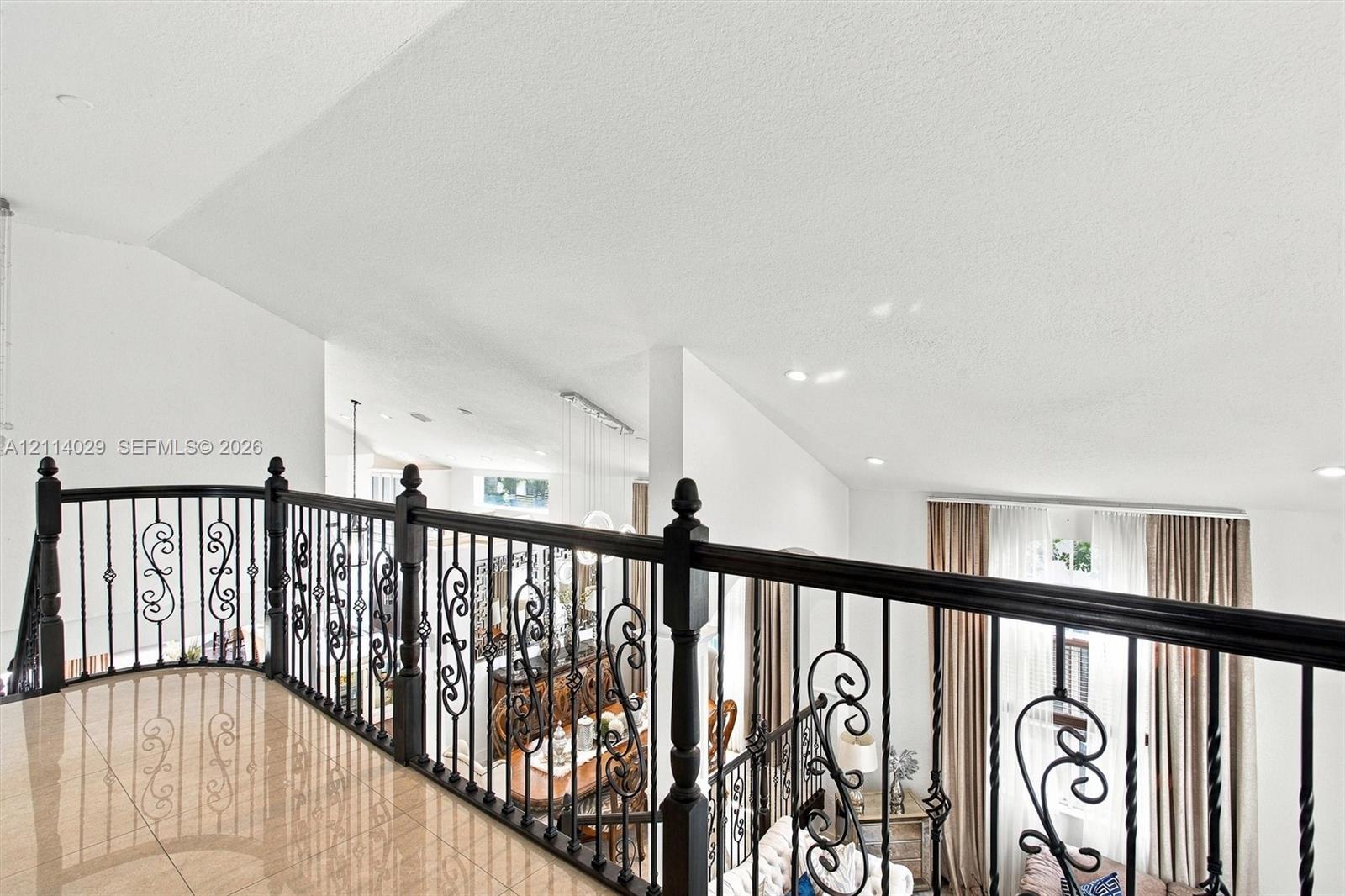 Interior landing featuring polished tile flooring, vaulted ceilings, and ornamental wrought iron balustrading with decorative scrollwork