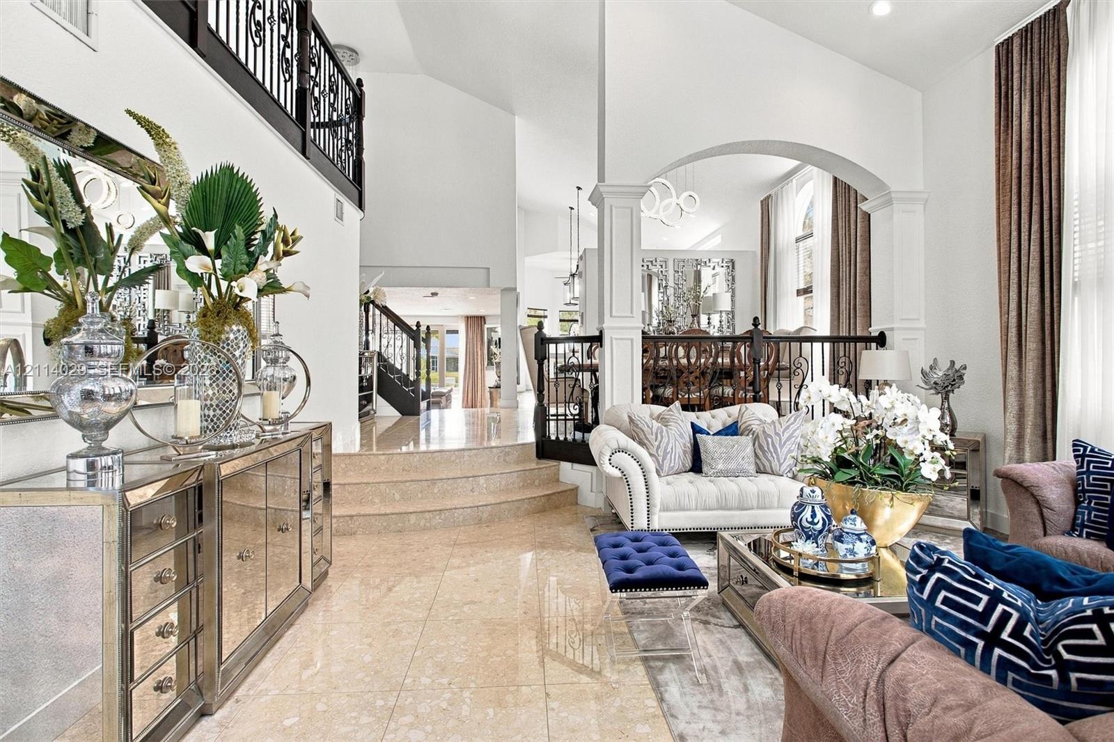 High-ceiling living area featuring stone tile flooring, an elevated platform, arched architectural detailing, and ornamental metal railings