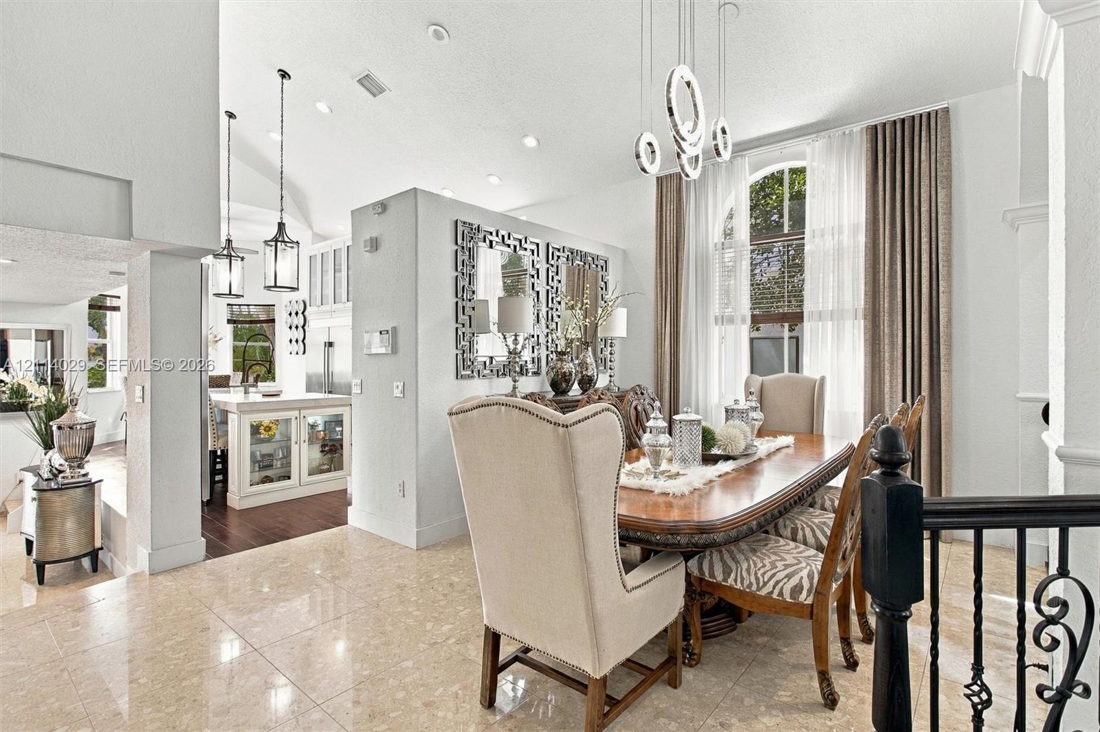 Open-concept dining area featuring vaulted ceilings, polished stone flooring, custom architectural recessed lighting, modern geometric pendant chandeliers, and an arched window