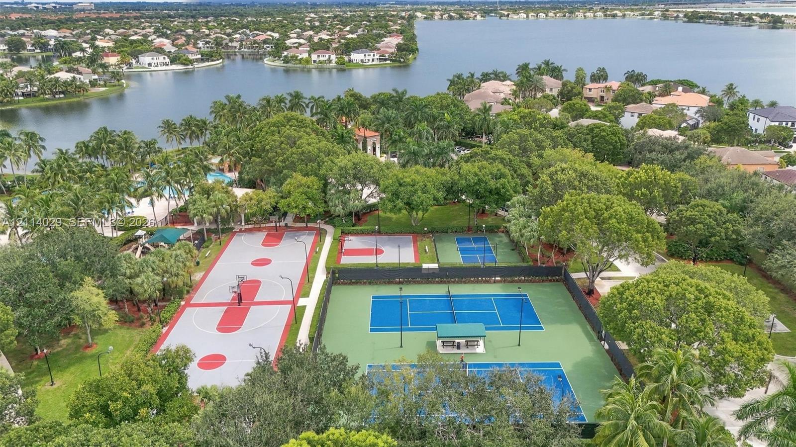 Recreational area featuring fenced tennis courts, a multi-sport court, and mature landscaping