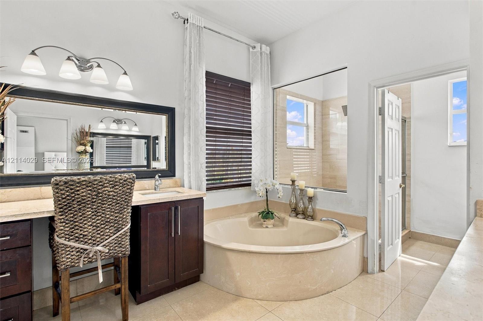 Built-in dark wood vanity with a stone countertop, oversized rectangular mirror, built-in soaking tub with stone surround, tile flooring, and integrated wall-to-wall mirror partitioning