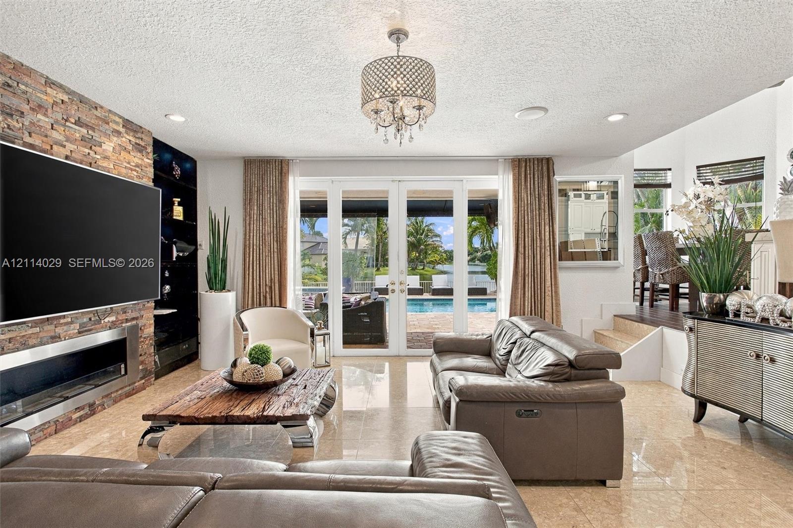 Stacked stone accent wall with integrated linear fireplace, polished stone flooring, and multi-panel glass doors opening to a pool area