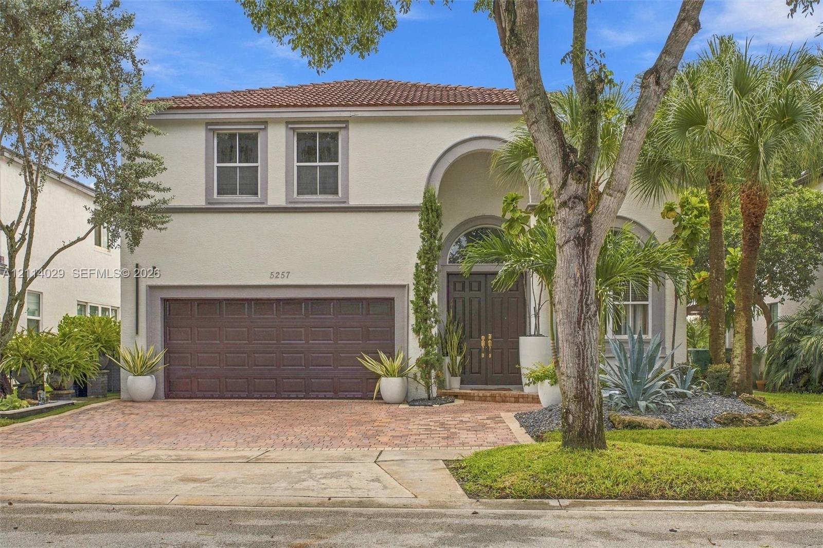 Two-story stucco exterior featuring a barrel tile roof, arched entryway with double doors, and a decorative stone-paved driveway