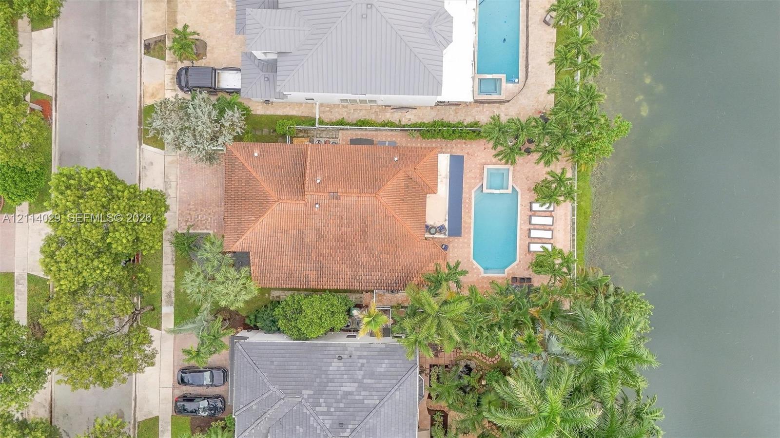 Waterfront property featuring a tile roof, an in-ground pool with an integrated spa, and an expansive paved patio