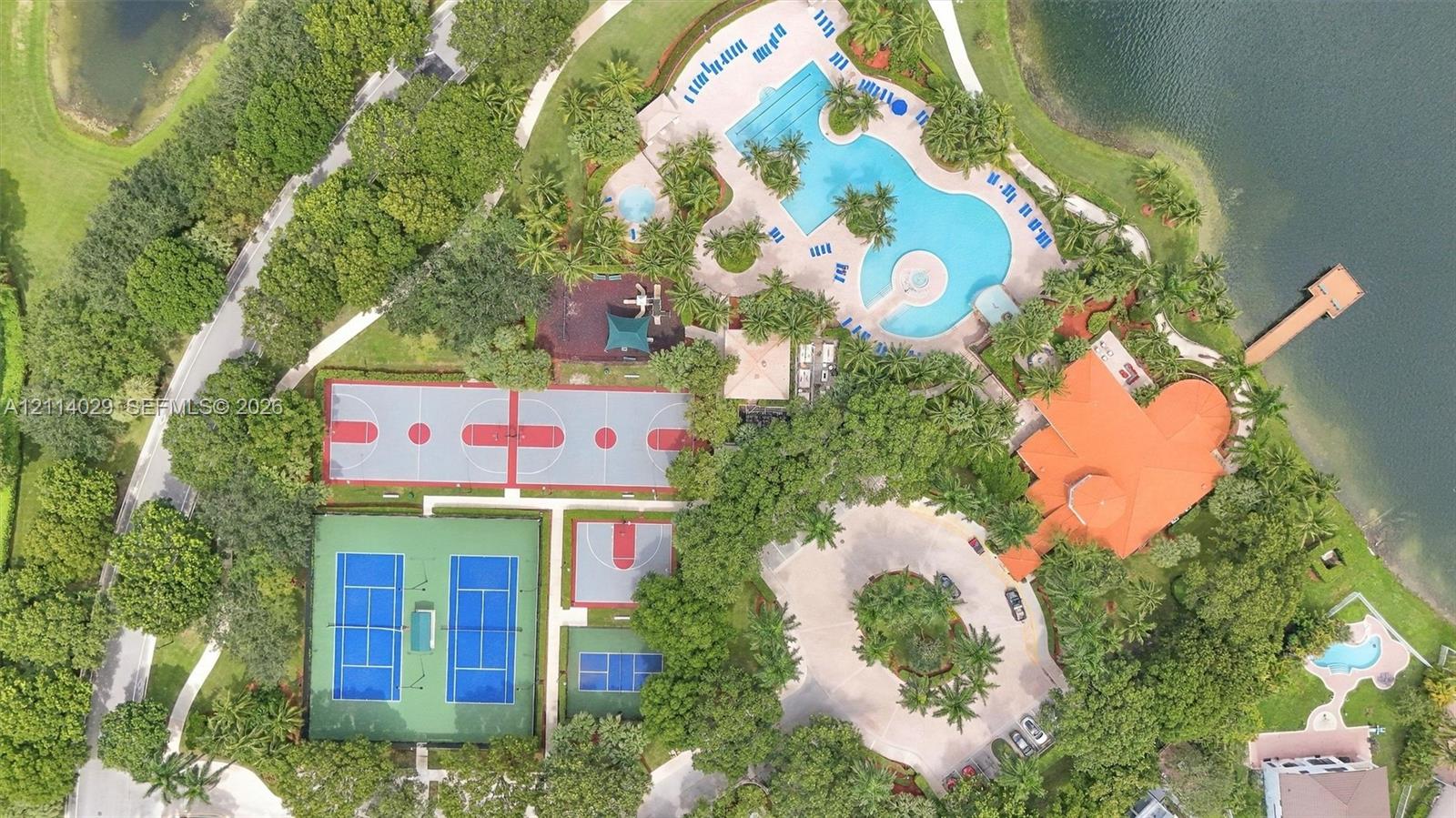 Aerial recreation complex featuring a resort-style swimming pool, two tennis courts, a basketball court, and a wooden lakefront dock