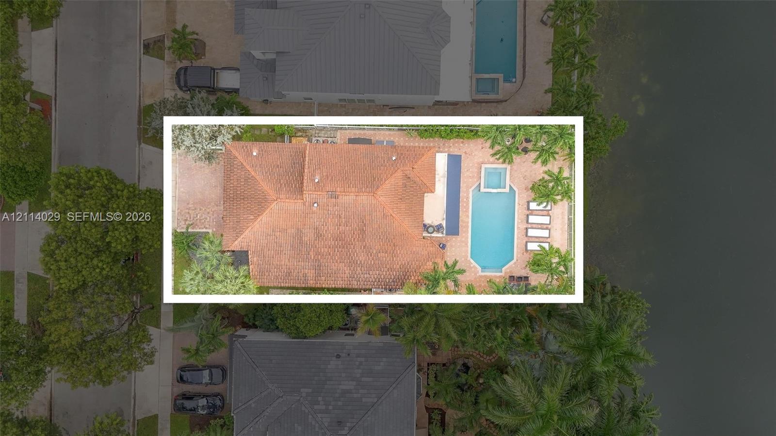 Aerial perspective of a property featuring a tile roof, paved patio, swimming pool, raised spa, and waterfront bulkhead