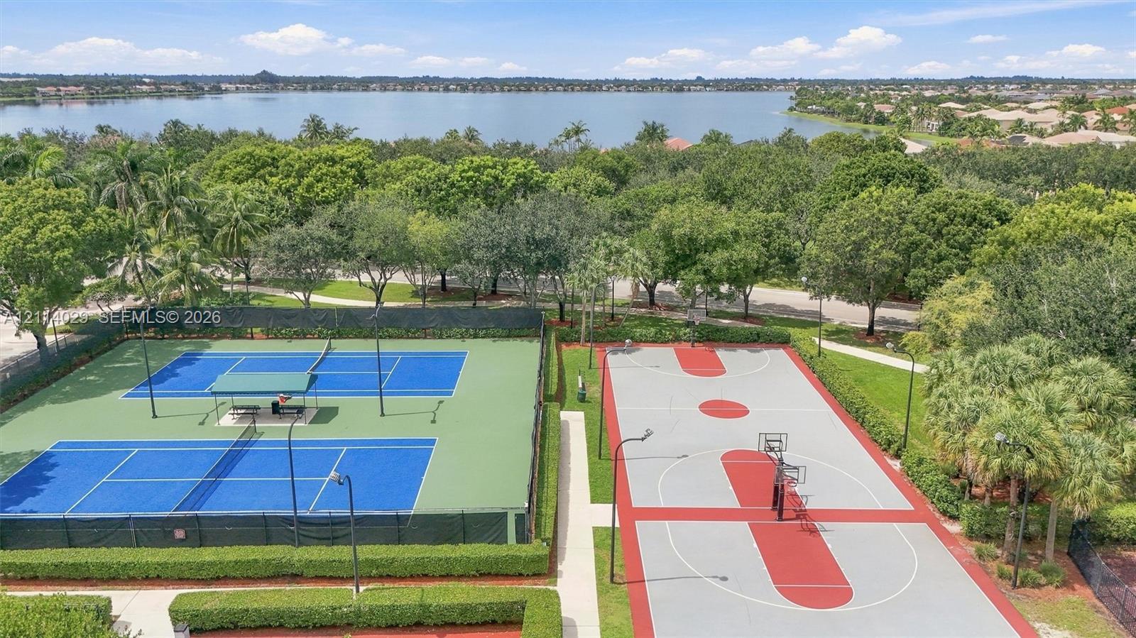 Community recreational area featuring two fenced tennis courts and a basketball court, surrounded by mature trees and proximity to a lake