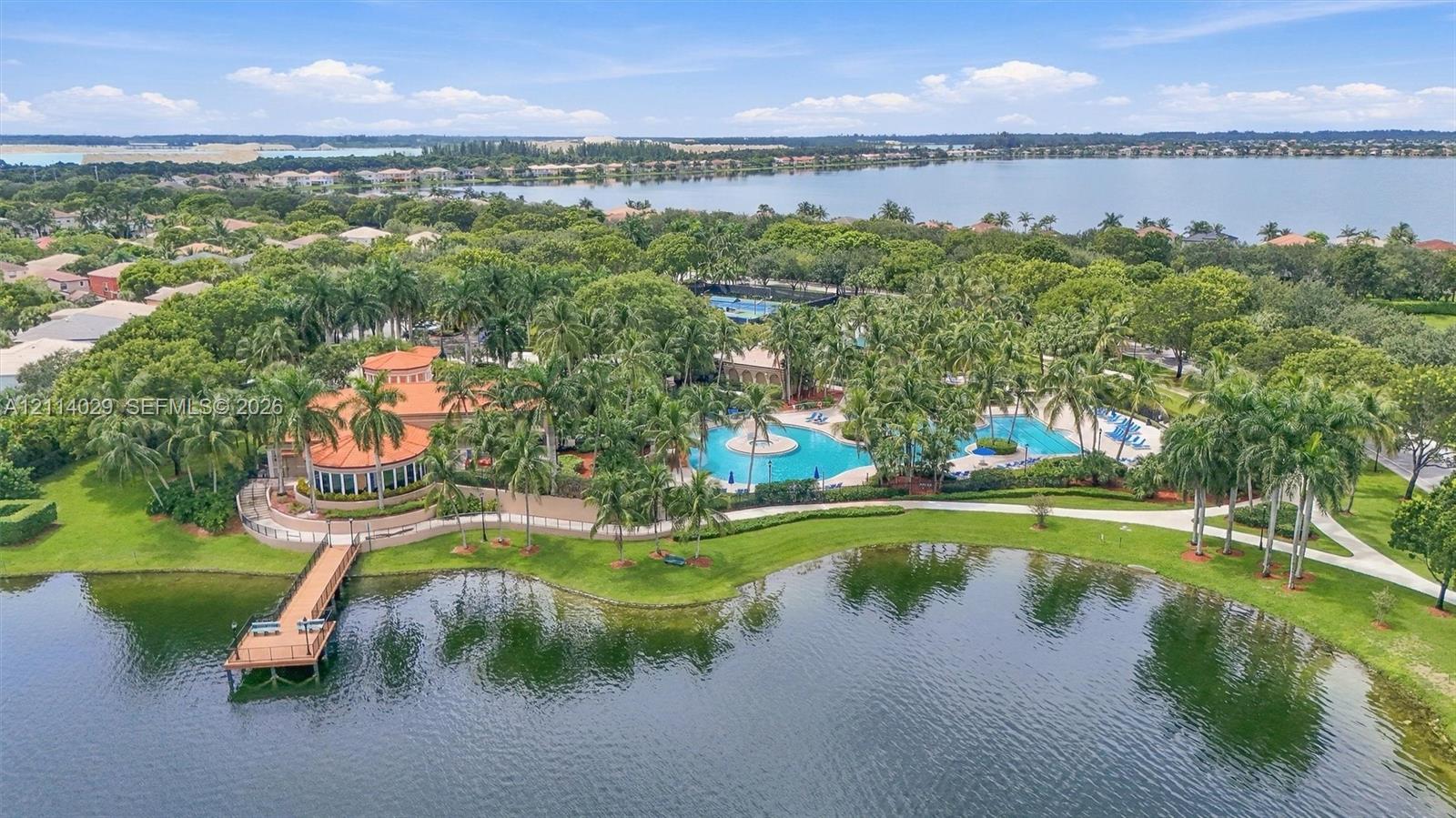 Waterfront community clubhouse featuring a swimming pool, pedestrian dock, manicured landscaping, and palm-lined grounds