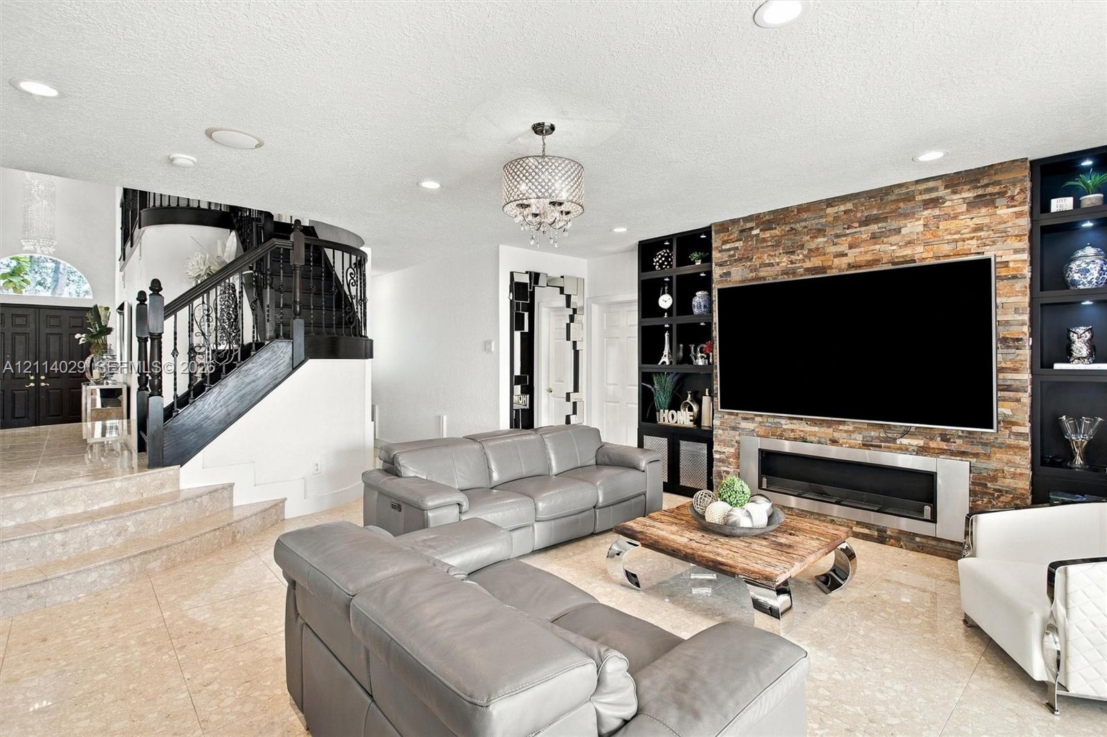Living area featuring stone-clad accent wall, linear fireplace, built-in black cabinetry, stone flooring, and staircase with black metal railing