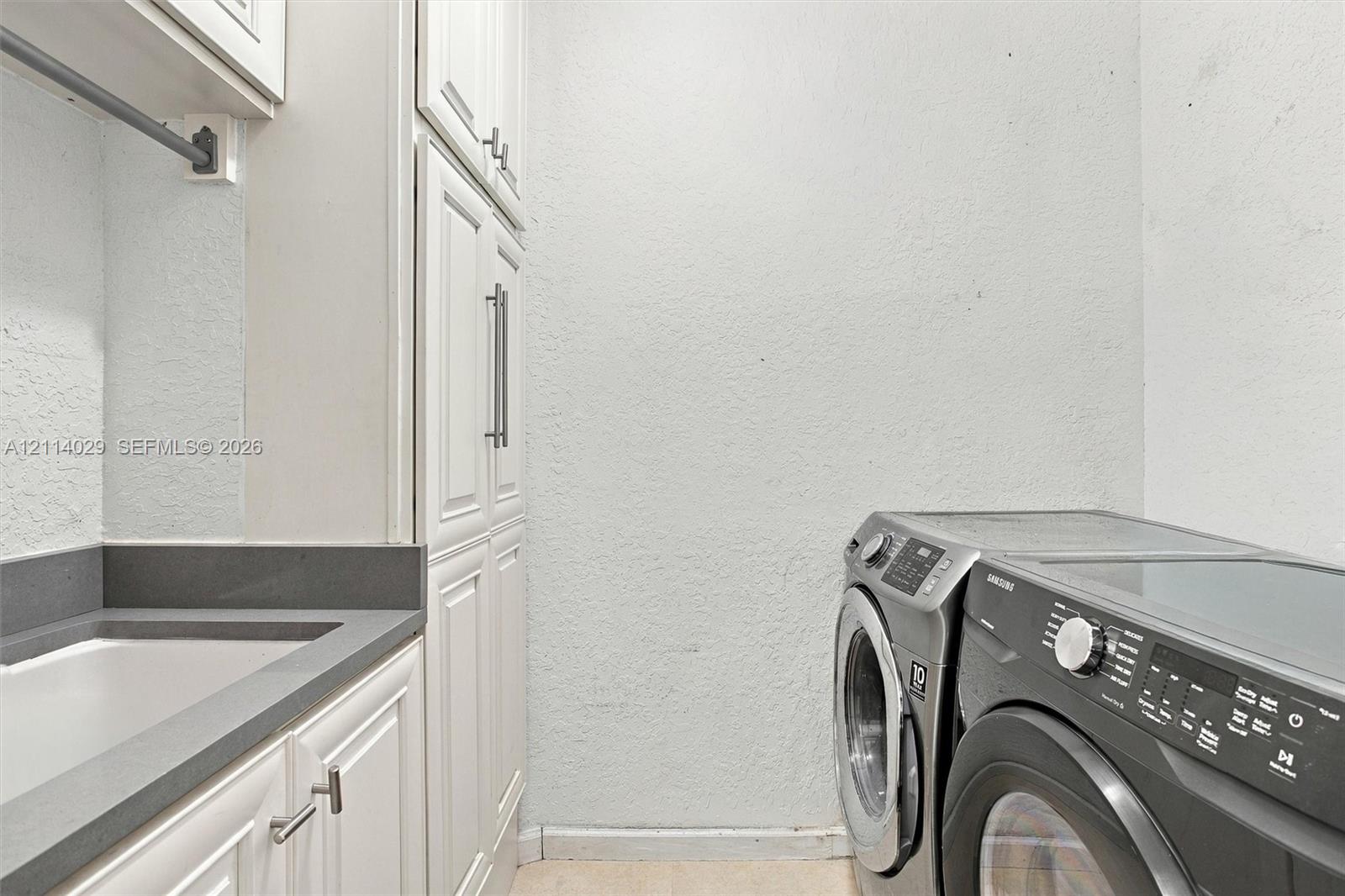 Laundry area featuring full-height white cabinetry, solid-surface countertop, integrated basin, and brushed nickel hardware