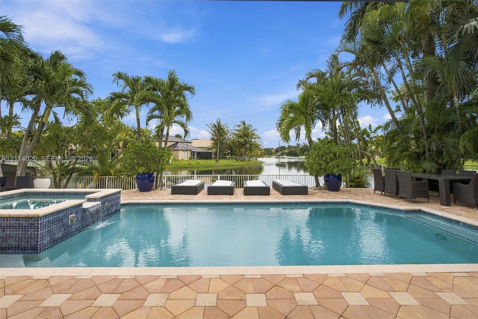 Outdoor pool area featuring a spillover spa with blue glass tile accents, stone paver decking, and waterfront positioning