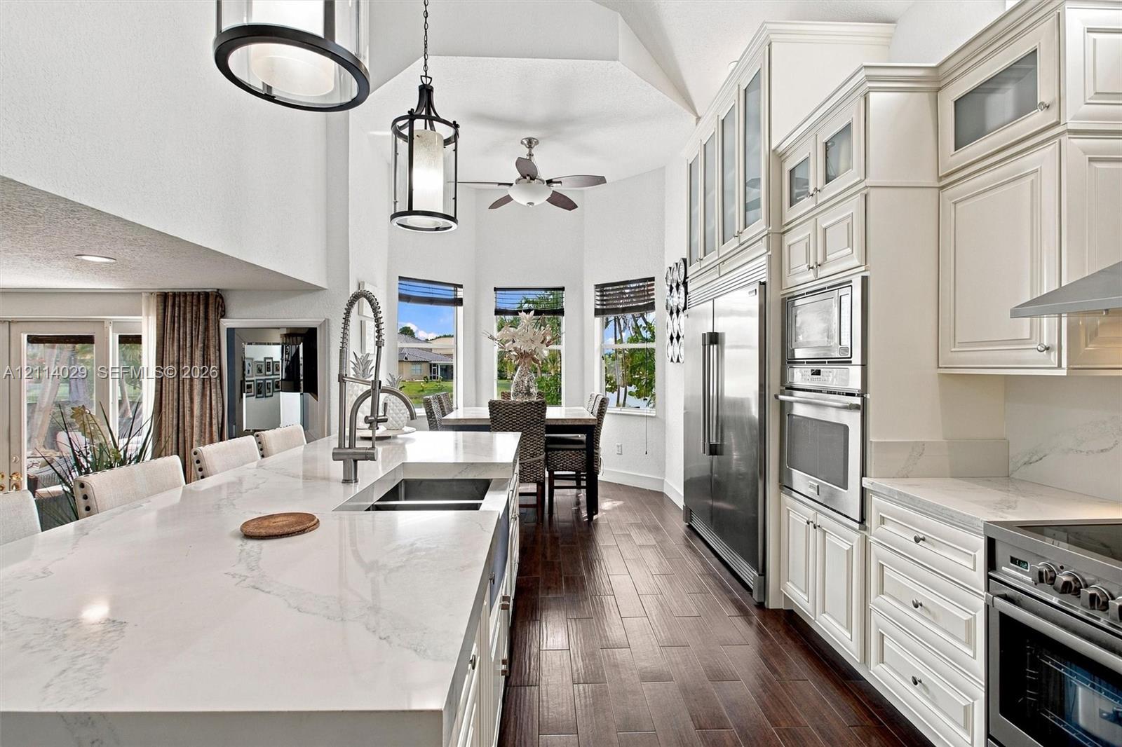 Kitchen featuring a quartz-topped island with an undermount sink, custom cabinetry with glass-front uppers, stainless steel built-in appliances, wood-finish flooring, and vaulted ceilings