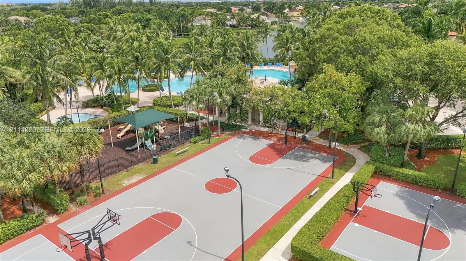 Community recreation area featuring multiple basketball courts, a swimming pool, and a playground area surrounded by mature palm trees and manicured landscaping