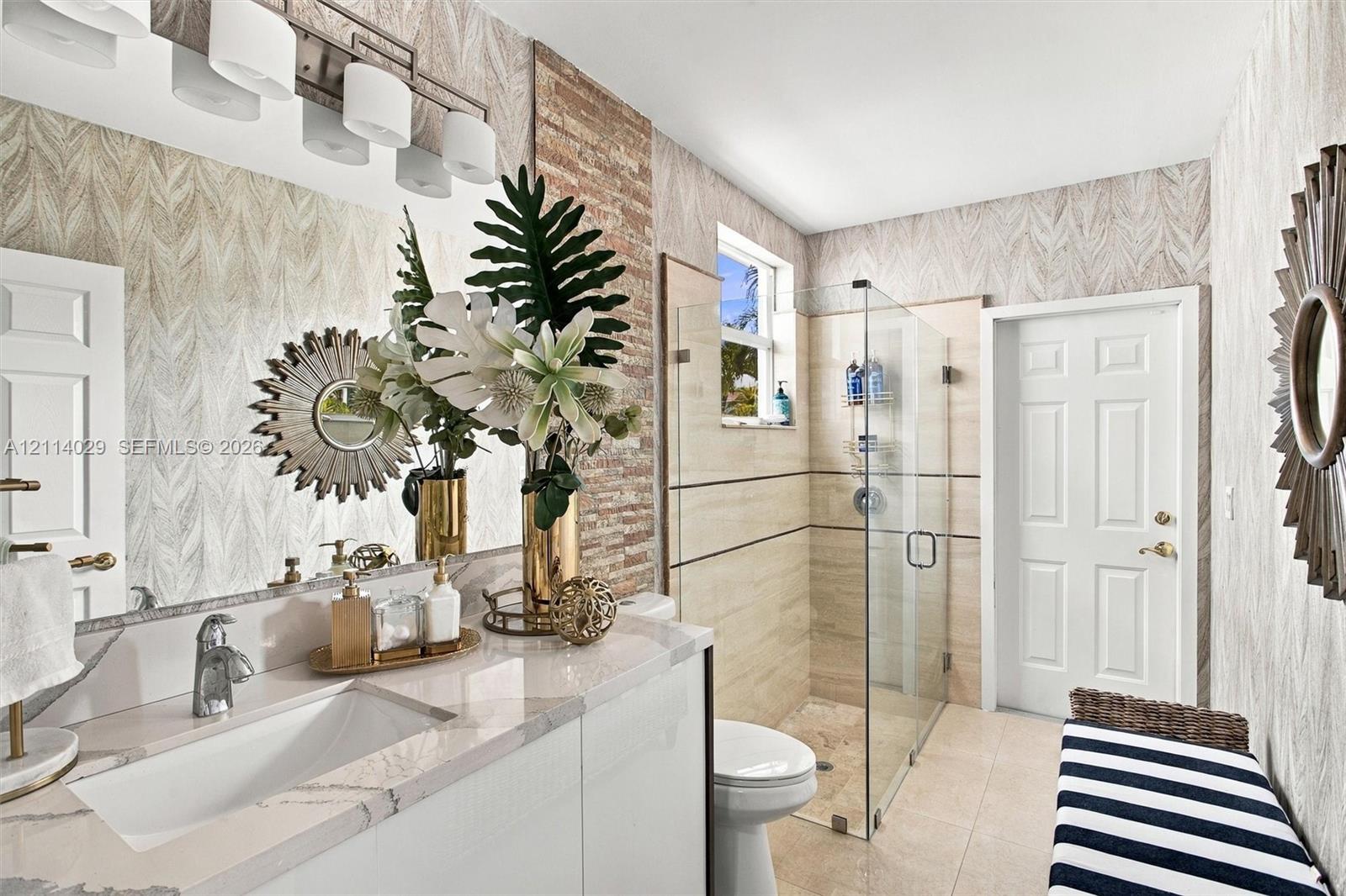 Bathroom featuring a vanity with a white countertop and rectangular undermount sink, glass-enclosed shower with horizontal accent tile, and textured wall treatment