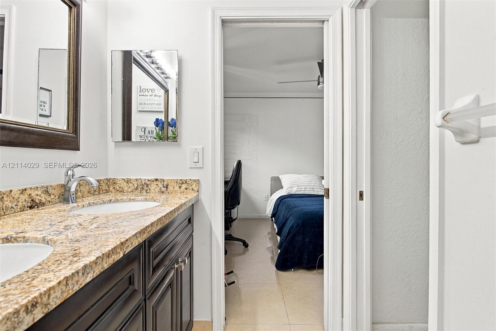 Double-sink vanity featuring dark-toned cabinetry, stone-finish countertops, wall-mounted mirror, and metal fixtures