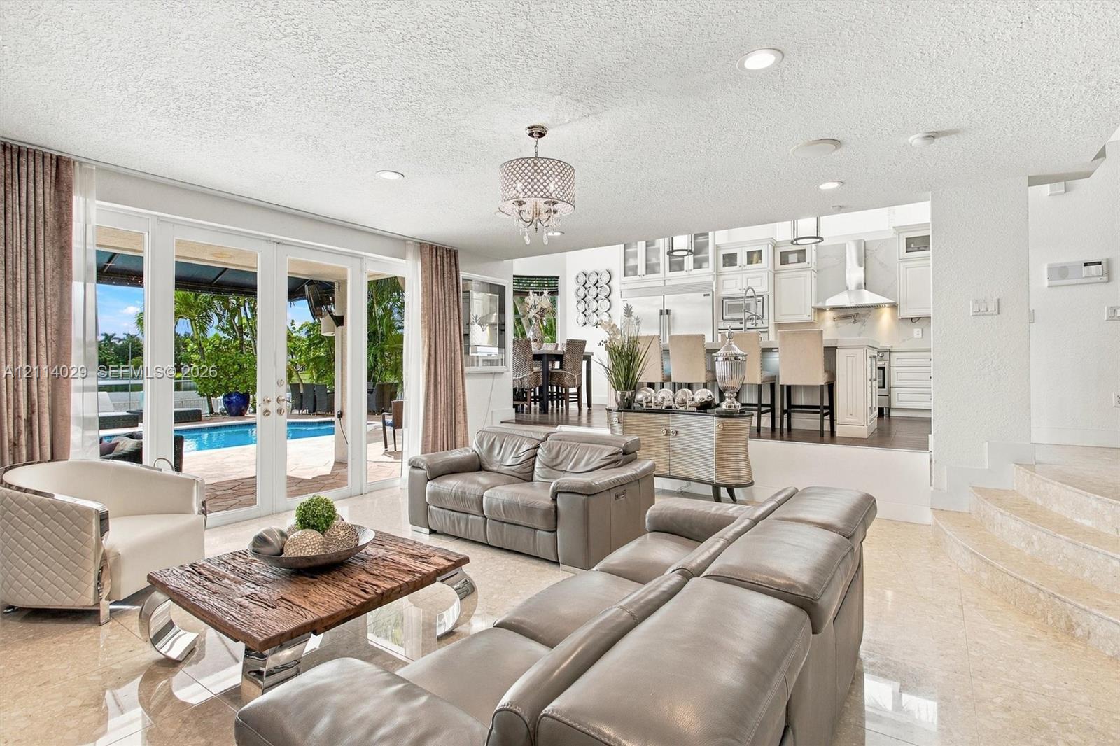 Open-concept floor plan featuring polished stone flooring, recessed lighting, white cabinetry, and multi-panel glass doors with exterior patio and pool access