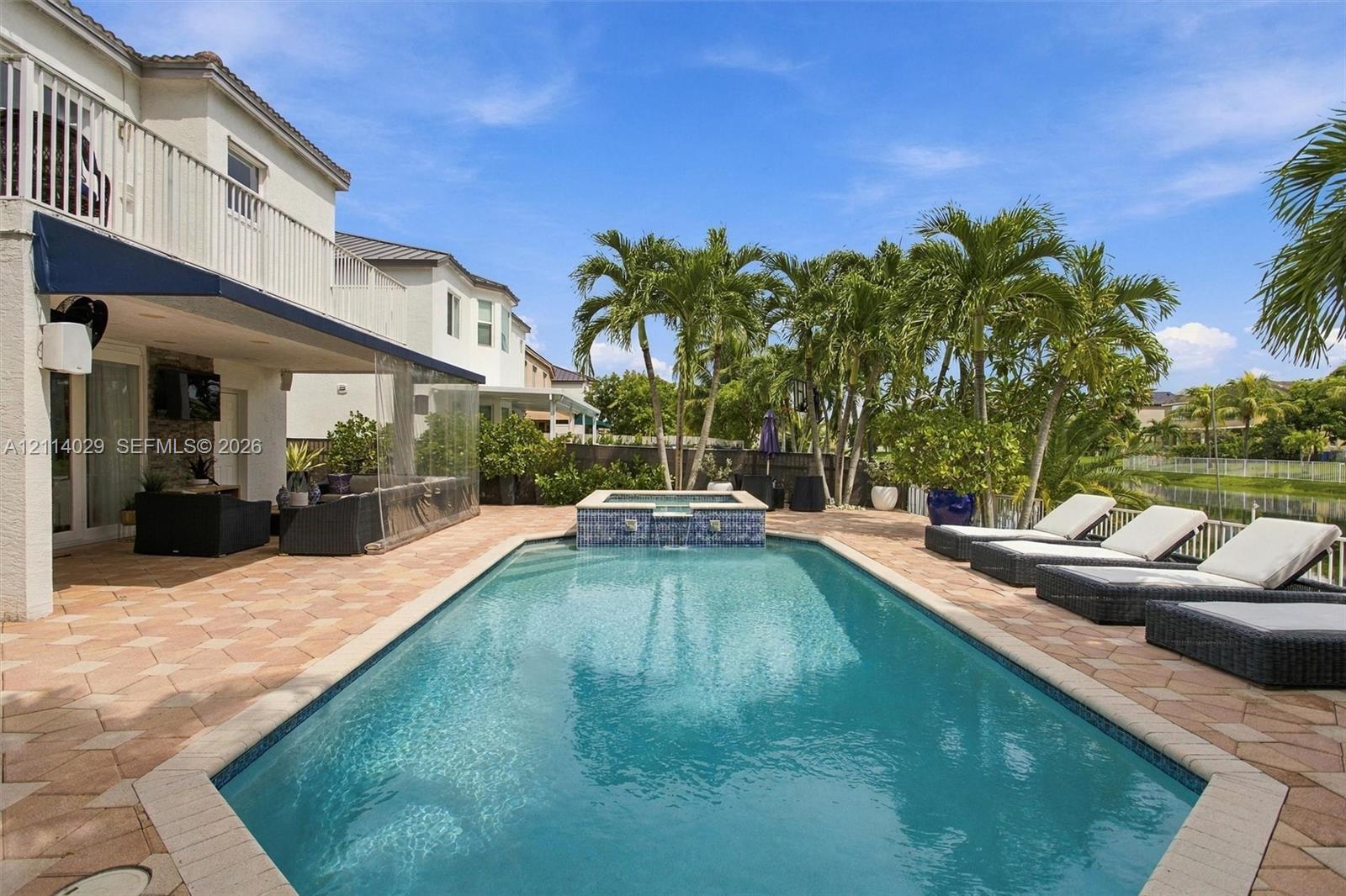 In-ground pool featuring a spillover spa with decorative tile inlay, set within a paved patio area under a covered lanai